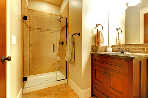 Bathroom with wood cabinet and tile shower with golden tone.